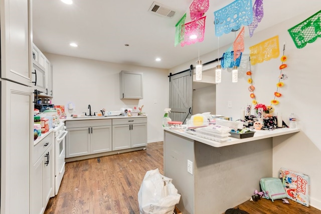 kitchen featuring kitchen peninsula, a barn door, light hardwood / wood-style flooring, white cabinets, and a breakfast bar area