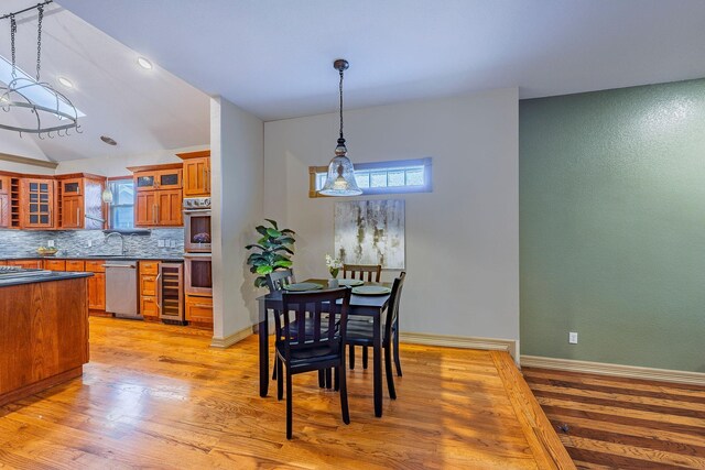 dining space with wine cooler, light hardwood / wood-style flooring, a wealth of natural light, and vaulted ceiling