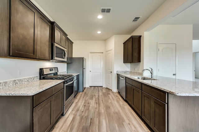 kitchen featuring sink, light hardwood / wood-style flooring, light stone countertops, appliances with stainless steel finishes, and dark brown cabinets