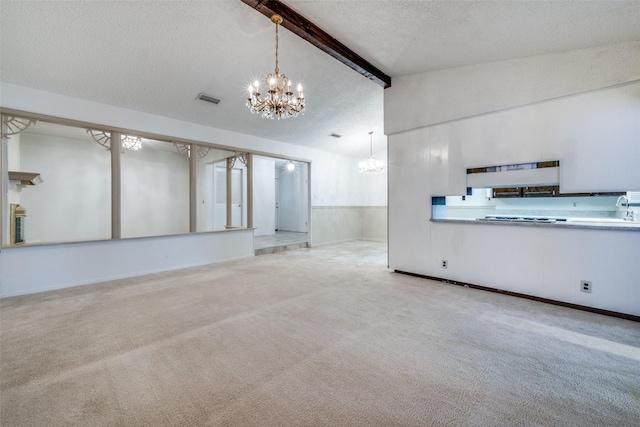 unfurnished living room featuring carpet flooring, beam ceiling, a textured ceiling, and an inviting chandelier