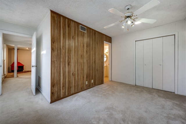 unfurnished bedroom featuring light carpet, a textured ceiling, ceiling fan, wooden walls, and a closet