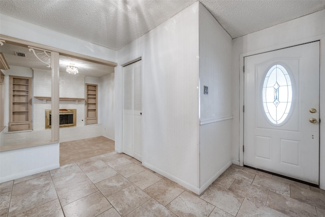 foyer entrance with a large fireplace, light tile patterned flooring, and a textured ceiling