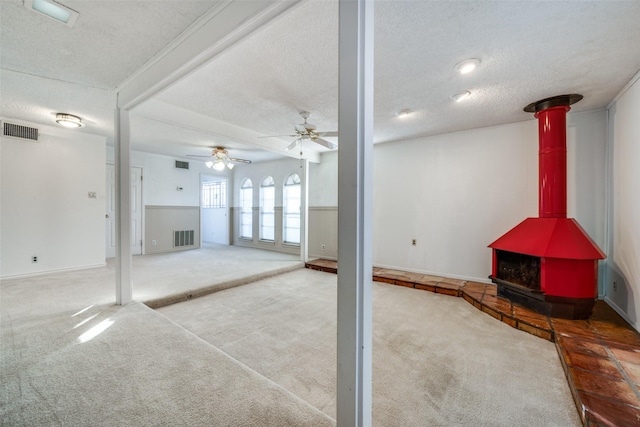 basement with carpet, a textured ceiling, a wood stove, and ceiling fan