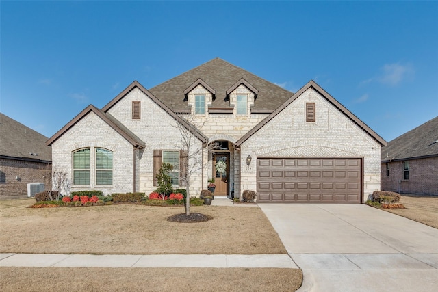 french country inspired facade featuring brick siding, cooling unit, roof with shingles, and concrete driveway