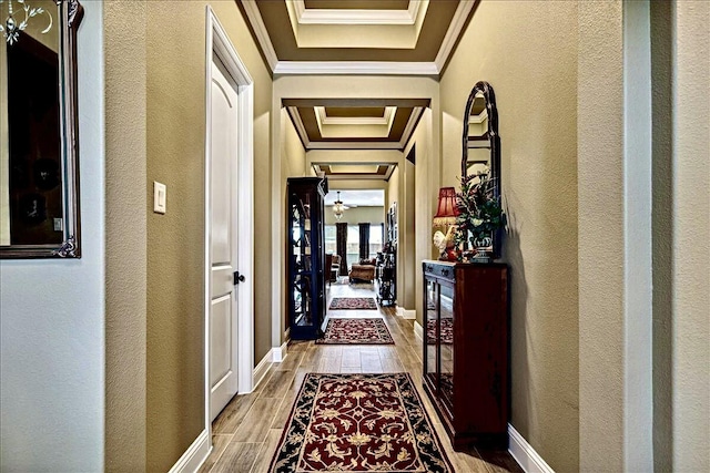 hall with crown molding, a textured wall, baseboards, and light wood-style flooring