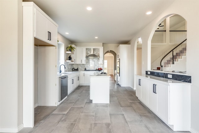 kitchen with dishwasher, wall chimney range hood, sink, a kitchen island, and white cabinetry