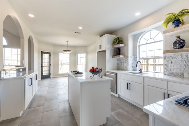 kitchen with stainless steel dishwasher, plenty of natural light, white cabinets, and sink