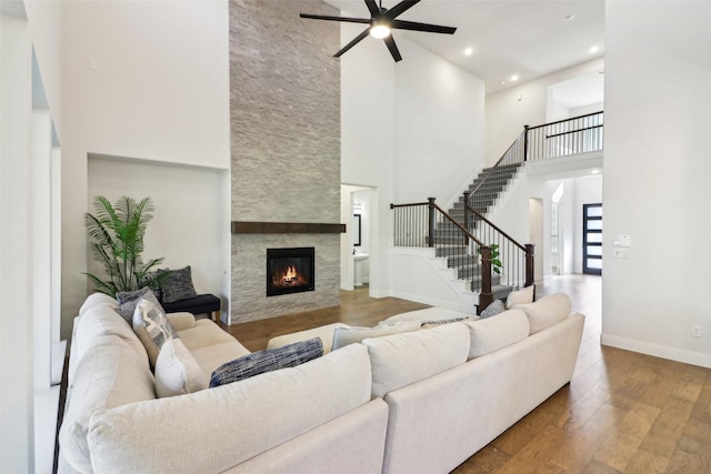 living room with hardwood / wood-style flooring, ceiling fan, a towering ceiling, and a fireplace