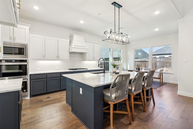 kitchen featuring appliances with stainless steel finishes, sink, hanging light fixtures, ceiling fan, and a center island with sink