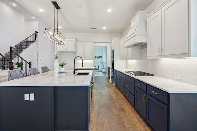 kitchen with an island with sink, white cabinets, and custom range hood