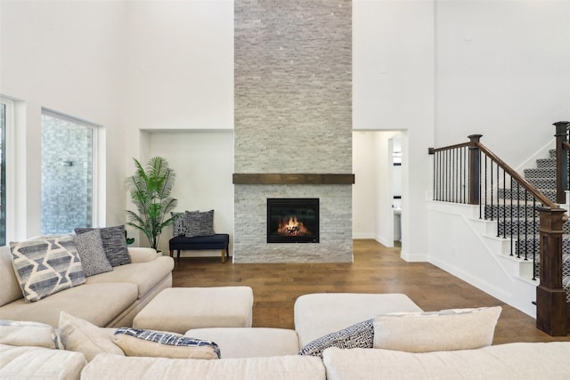 living room with a high ceiling, dark hardwood / wood-style flooring, and a stone fireplace