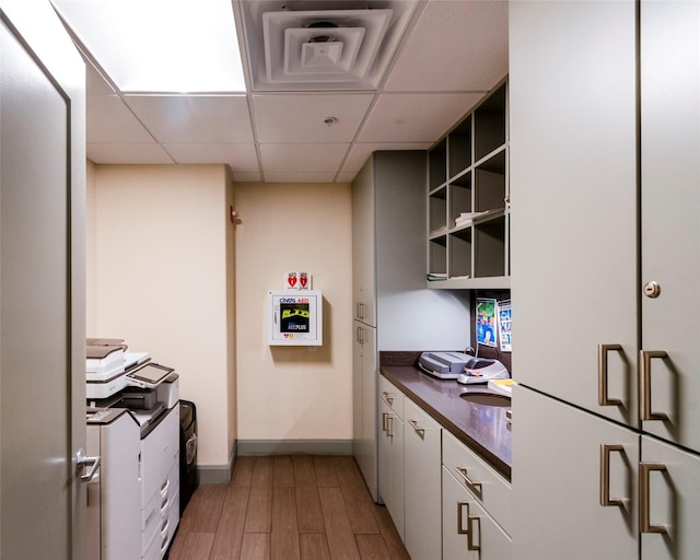 kitchen with wood-type flooring, a paneled ceiling, and white cabinets