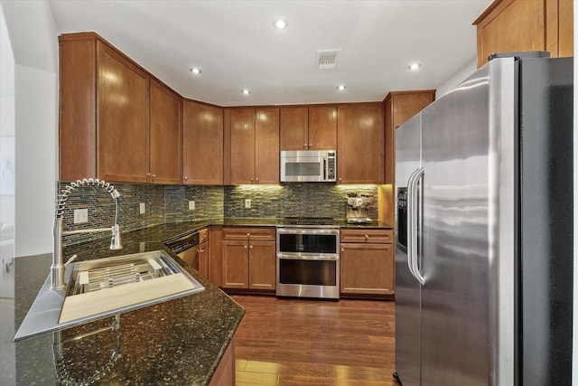 kitchen featuring sink, dark wood-type flooring, appliances with stainless steel finishes, backsplash, and dark stone counters