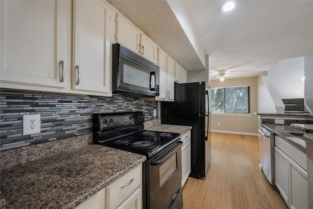 kitchen with dark stone counters, white cabinetry, black appliances, and light hardwood / wood-style floors