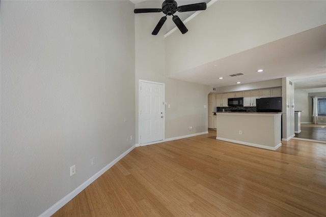 unfurnished living room featuring ceiling fan, a high ceiling, and light wood-type flooring