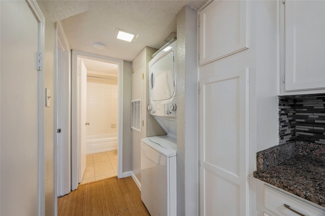 laundry area with a textured ceiling, stacked washer and dryer, and light hardwood / wood-style flooring