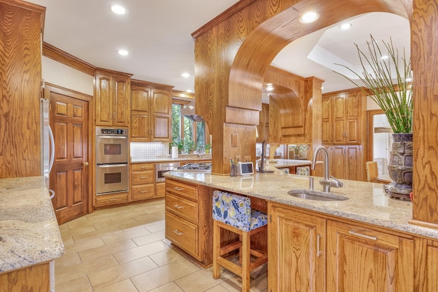 kitchen featuring stainless steel double oven, light stone counters, and sink