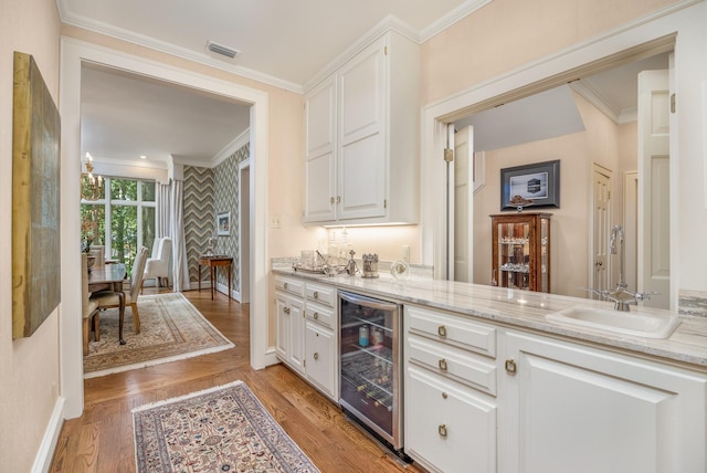 bar featuring sink, light stone countertops, light hardwood / wood-style floors, white cabinetry, and beverage cooler