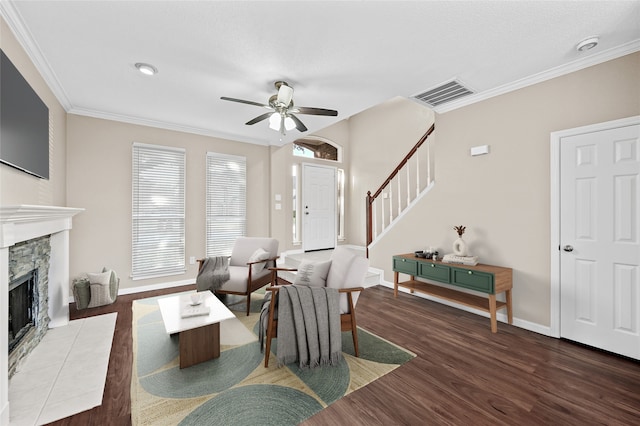 living room featuring ceiling fan, dark hardwood / wood-style flooring, ornamental molding, and a stone fireplace