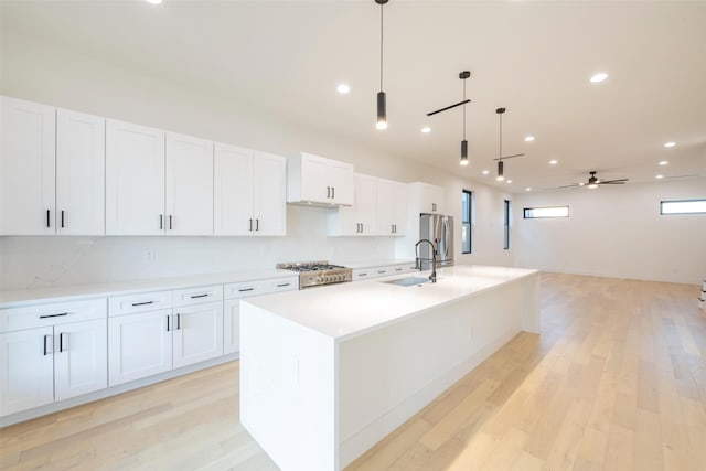 kitchen with ceiling fan, white cabinets, a center island with sink, and pendant lighting