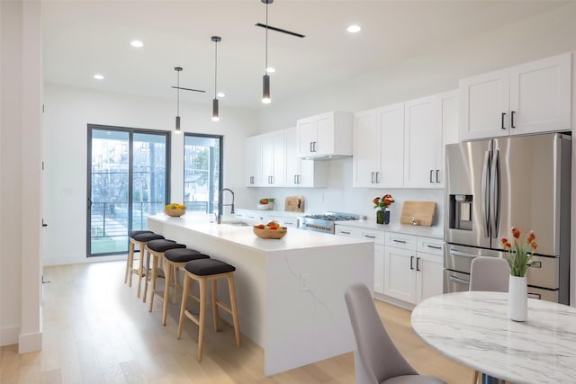 kitchen featuring stainless steel refrigerator with ice dispenser, white cabinetry, hanging light fixtures, and a kitchen island with sink