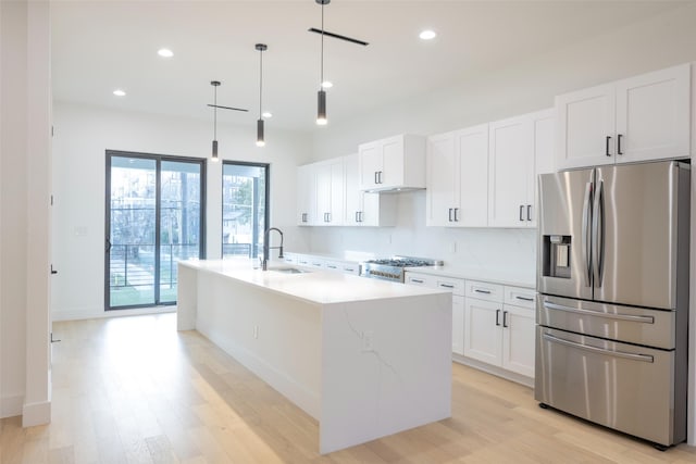 kitchen featuring white cabinetry, stainless steel fridge, a kitchen island with sink, decorative light fixtures, and sink