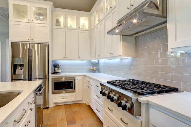 kitchen featuring light wood-type flooring, stainless steel appliances, white cabinetry, and backsplash