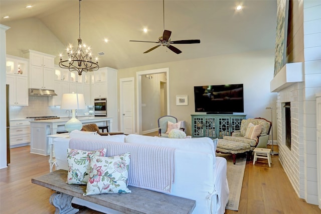 living room with ceiling fan with notable chandelier, a fireplace, high vaulted ceiling, and light hardwood / wood-style flooring