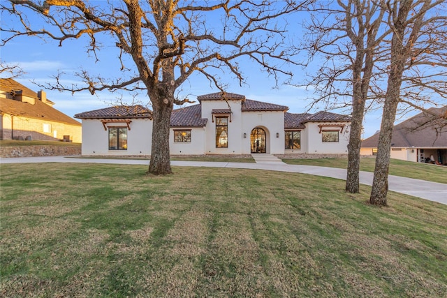 mediterranean / spanish-style home featuring driveway, a front lawn, a tiled roof, and stucco siding