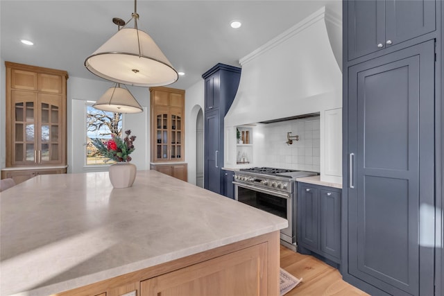 kitchen with arched walkways, custom exhaust hood, stainless steel stove, light countertops, and decorative backsplash