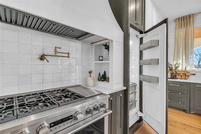 kitchen featuring stainless steel gas stove, light wood-type flooring, light countertops, and decorative backsplash