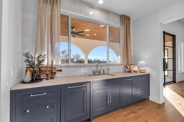 bar with light wood-style floors, baseboards, backsplash, and a sink