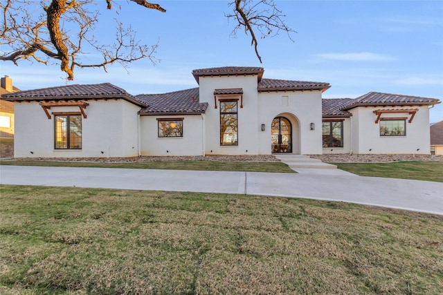 mediterranean / spanish house with a tiled roof, a front lawn, and stucco siding