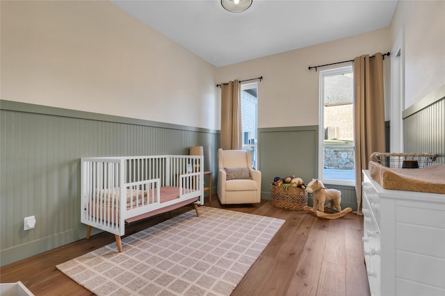 bedroom with vaulted ceiling, wainscoting, and wood-type flooring