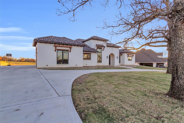 mediterranean / spanish-style home featuring a front yard, driveway, a tiled roof, and stucco siding