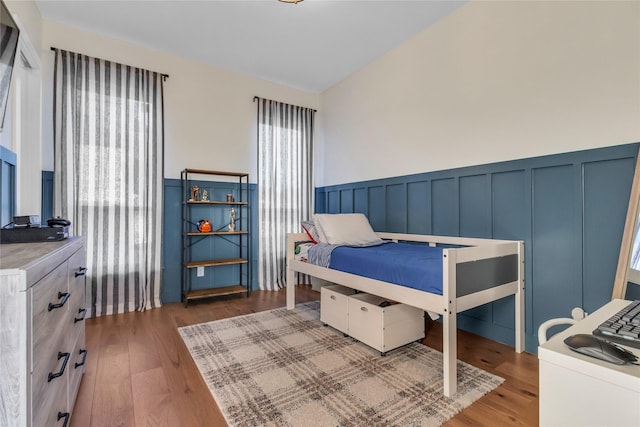 bedroom featuring a decorative wall, wood finished floors, and wainscoting