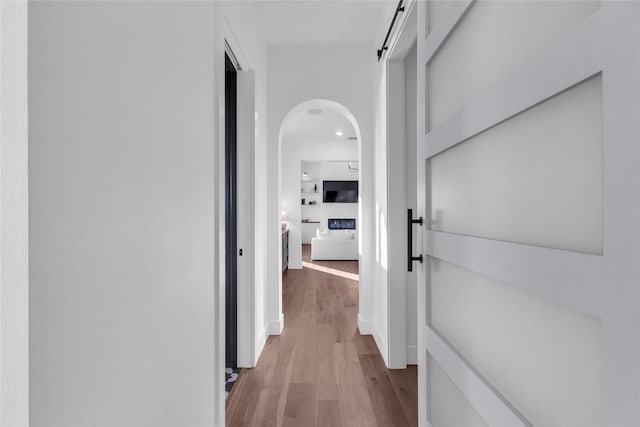 corridor featuring arched walkways, wood finished floors, and a barn door