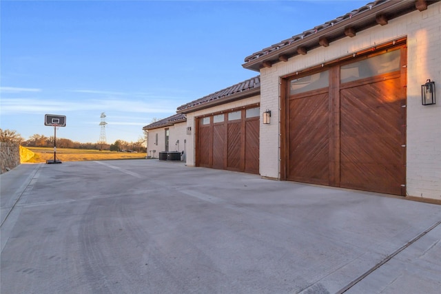 exterior space with a garage, brick siding, a tiled roof, and central air condition unit