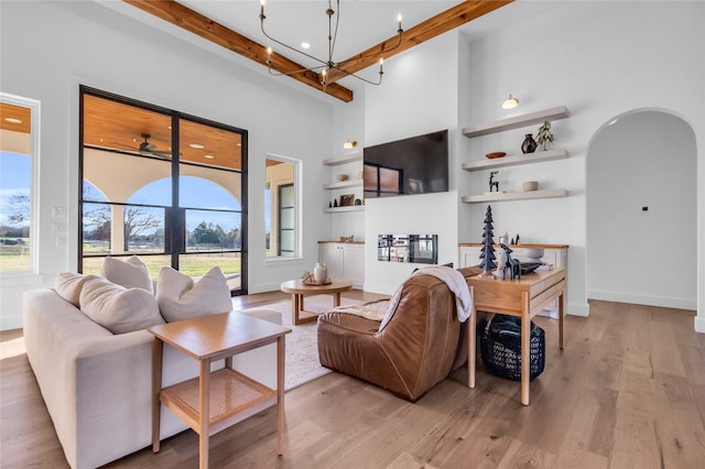 living room with beam ceiling, an inviting chandelier, a towering ceiling, and light hardwood / wood-style flooring