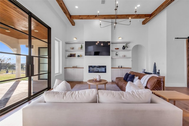 living area featuring arched walkways, an inviting chandelier, a glass covered fireplace, wood finished floors, and beamed ceiling