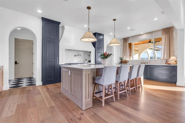 kitchen with a breakfast bar area, a kitchen island, light countertops, light wood-type flooring, and decorative backsplash