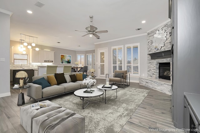 living room with ceiling fan, sink, a stone fireplace, light hardwood / wood-style floors, and ornamental molding