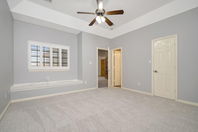 unfurnished bedroom featuring light carpet, a tray ceiling, and ceiling fan