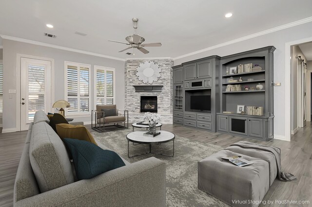 living room with ceiling fan, a stone fireplace, wood-type flooring, and crown molding