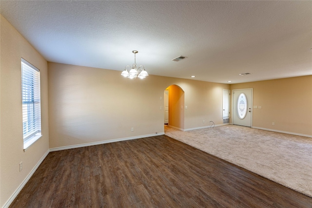 unfurnished room with a notable chandelier, dark wood-type flooring, and a textured ceiling