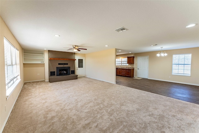 unfurnished living room featuring carpet floors, ceiling fan with notable chandelier, a large fireplace, and a textured ceiling