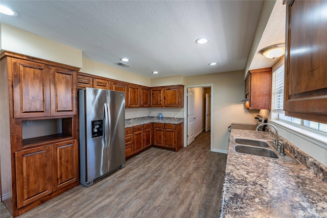 kitchen with sink, appliances with stainless steel finishes, a textured ceiling, dark hardwood / wood-style flooring, and dark stone counters