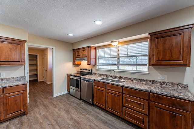 kitchen featuring sink, hardwood / wood-style flooring, stainless steel appliances, a textured ceiling, and dark stone counters