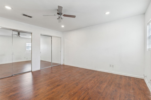 unfurnished bedroom with two closets, ceiling fan, and dark hardwood / wood-style floors