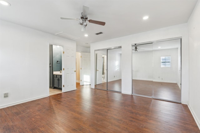 unfurnished bedroom featuring hardwood / wood-style floors, connected bathroom, two closets, and ceiling fan